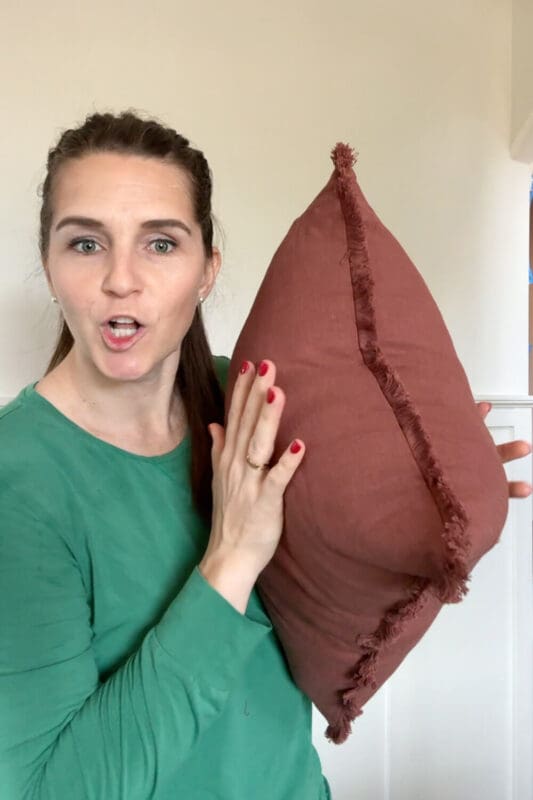 Demonstrating a rust pillow with fringe and a sized-up insert to add color and texture to a formal living room.