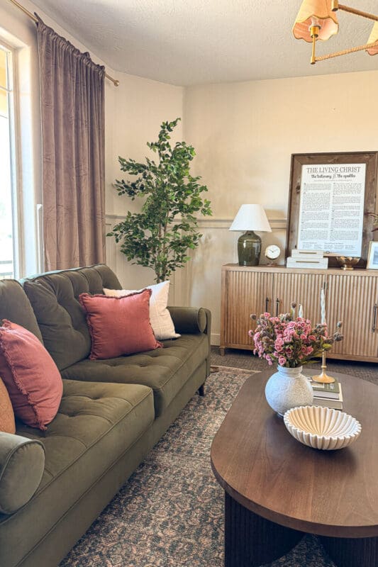 Formal living room with solid taupe curtains, green sofa, vintage-style rug, and brass chandelier demonstrating a darker, more tailored curtain option.