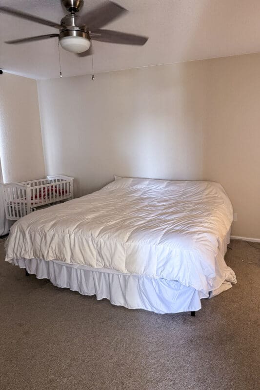guest room before the refresh with plain white comforter, bed skirt, and empty wall
