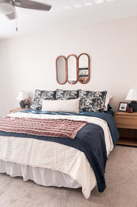 guest room refresh with cozy fall bedding, navy quilt layered over cream duvet, rust knit throw, patterned euro pillows, gingham lumbar, wood nightstands, triple wood mirror
