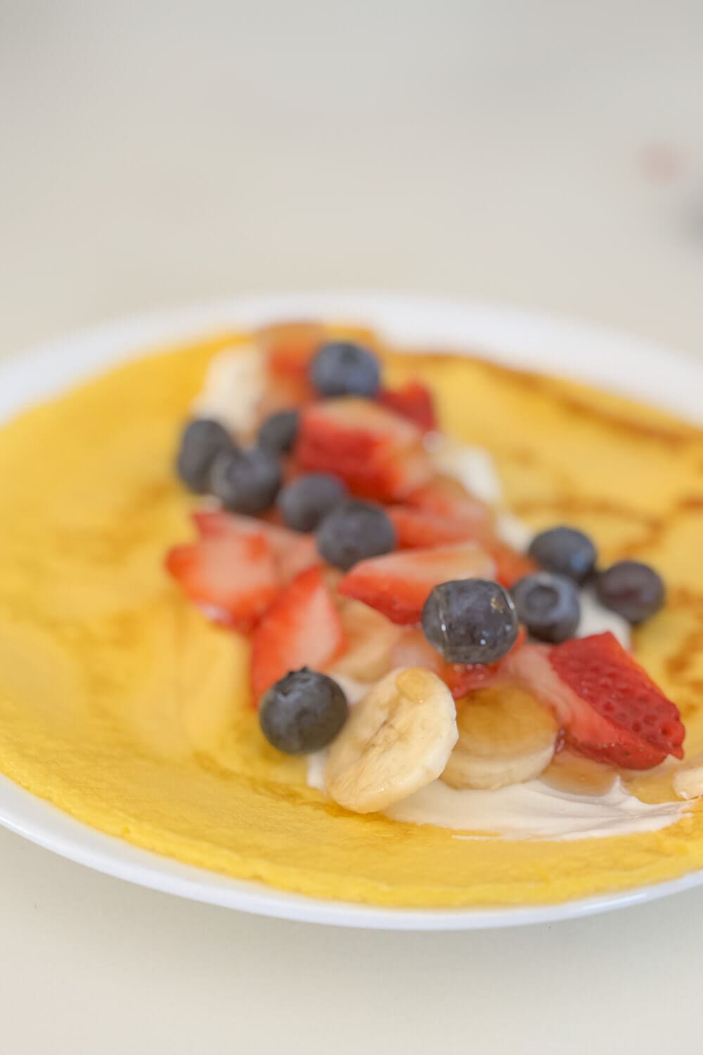 Crepe topped with strawberries, blueberries, bananas, and yogurt—ready to roll.