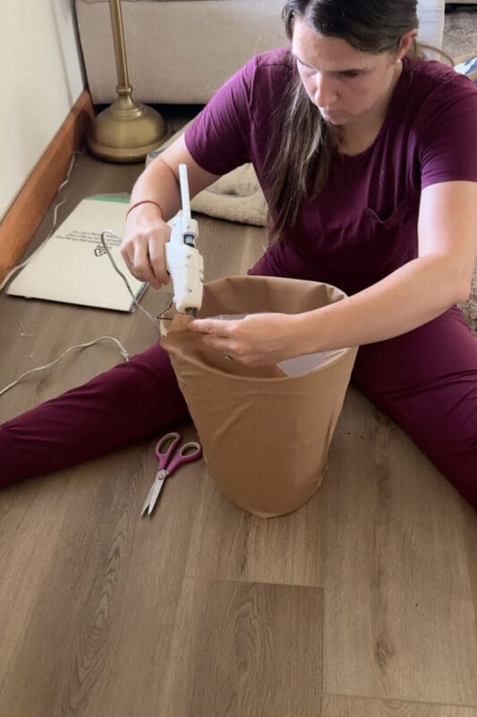Hot gluing the top edge of brown fabric to the poster-board cylinder to finish the flower-pot skirt for a kids no sew cardstock flower costume.