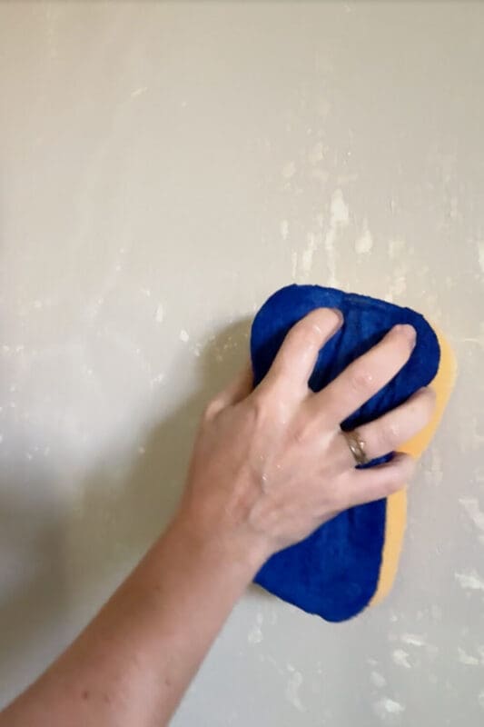 Wiping with a damp sponge to smooth joint compound on drywall.