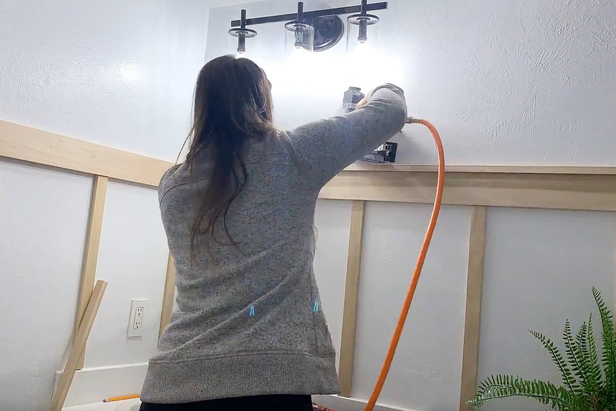 Attaching the top cap trim near the vanity light with a brad nailer to finish a DIY board and batten bathroom wall.