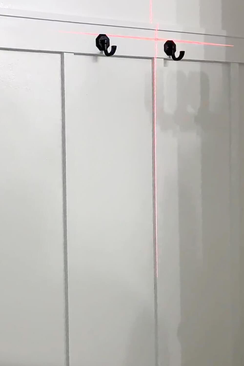 White board and batten bathroom wall with black hooks along the top rail, laser line aligning the hardware.