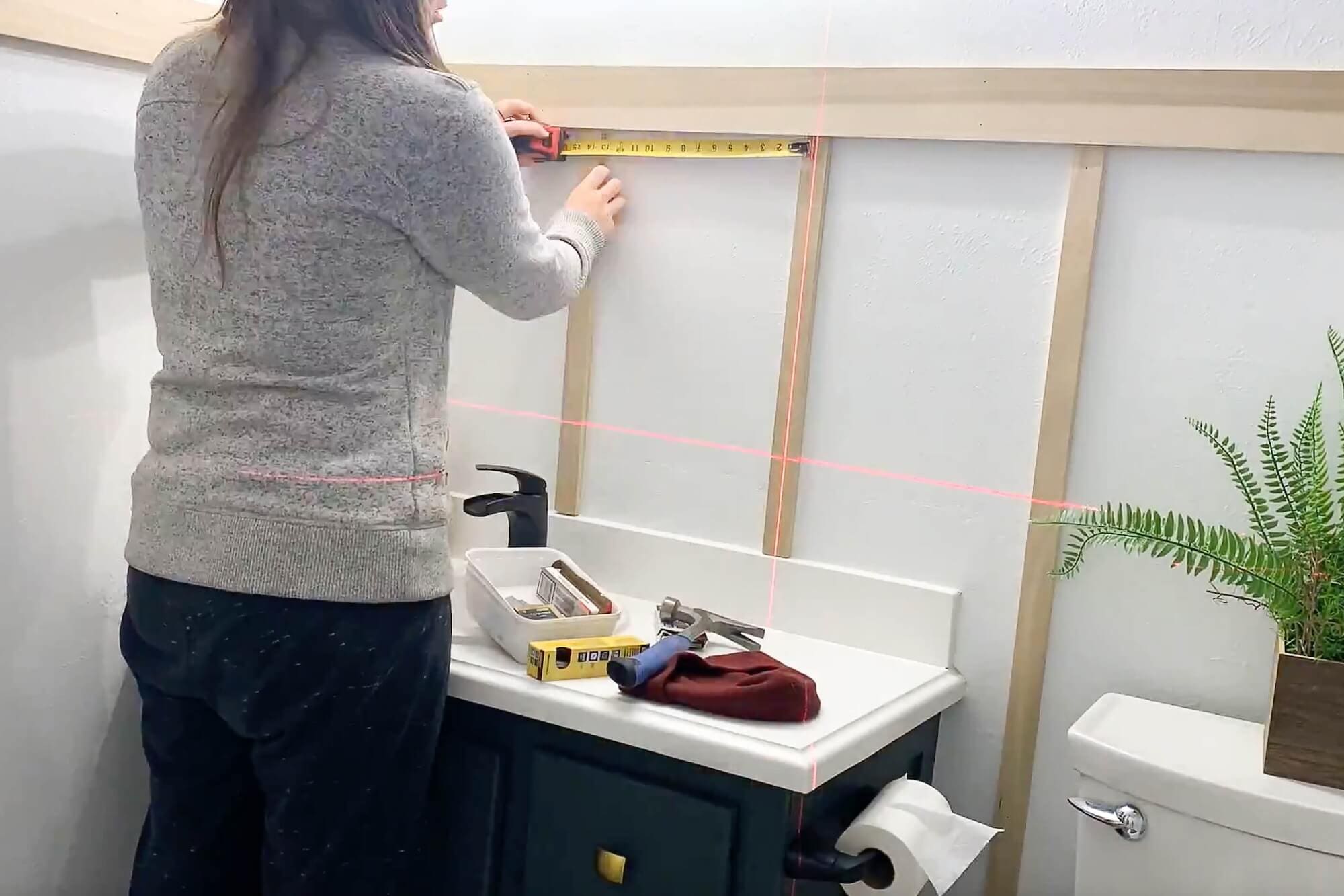 Using a laser level to mark spacing for vertical 1x2 battens above the vanity for a DIY board and batten wall.