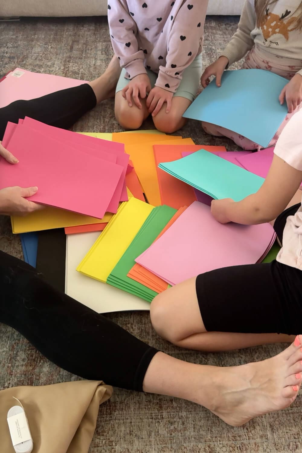 Kids sorting stacks of bright cardstock for a DIY Halloween project—pink, yellow, green, blue sheets ready to cut into petals for a quick, inexpensive DIY.