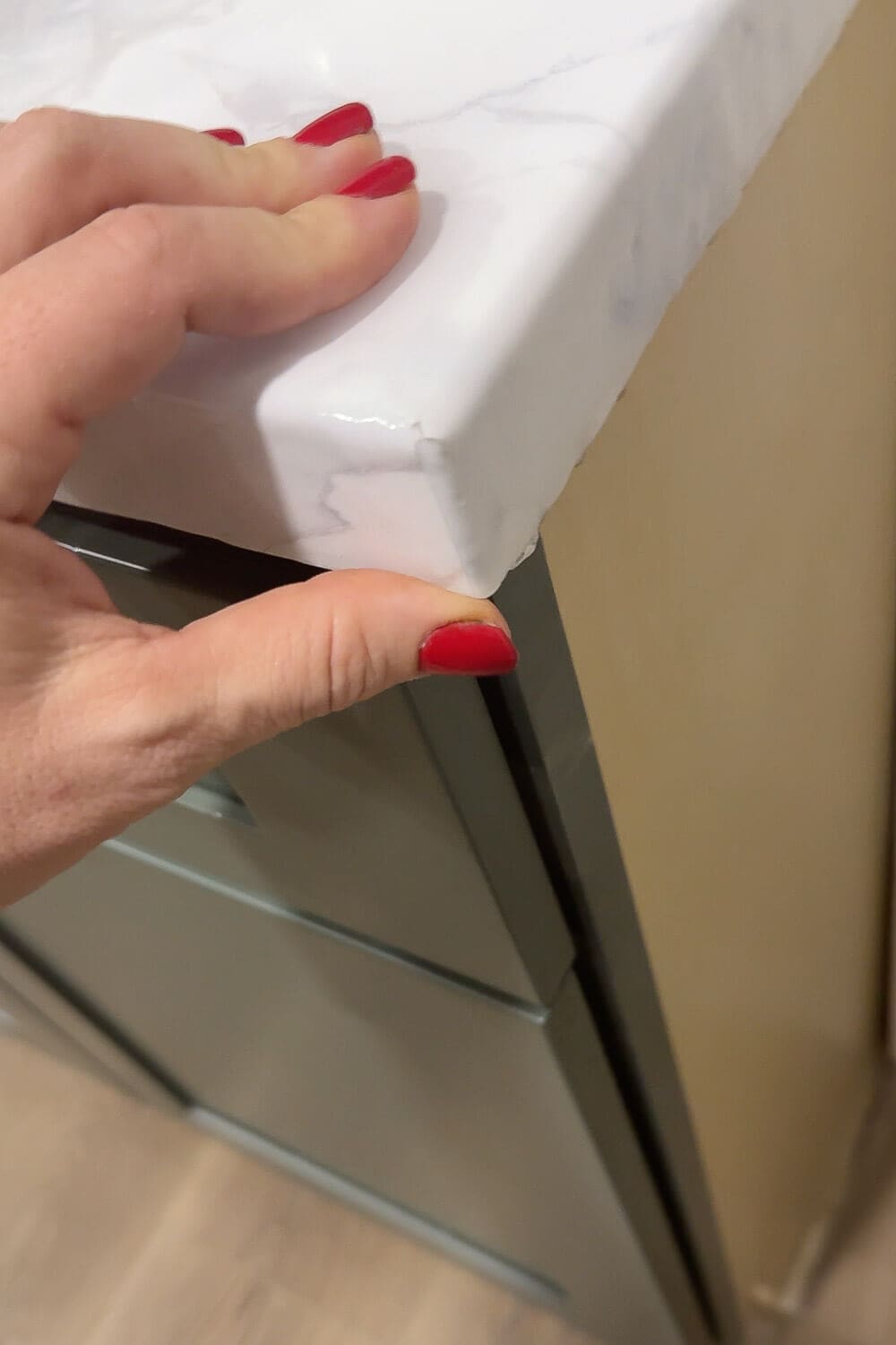 Close-up of an outside corner on a DIY faux marble countertop, showing how marble contact paper is wrapped smoothly around the edge while a hand with red nail polish holds the corner in place.