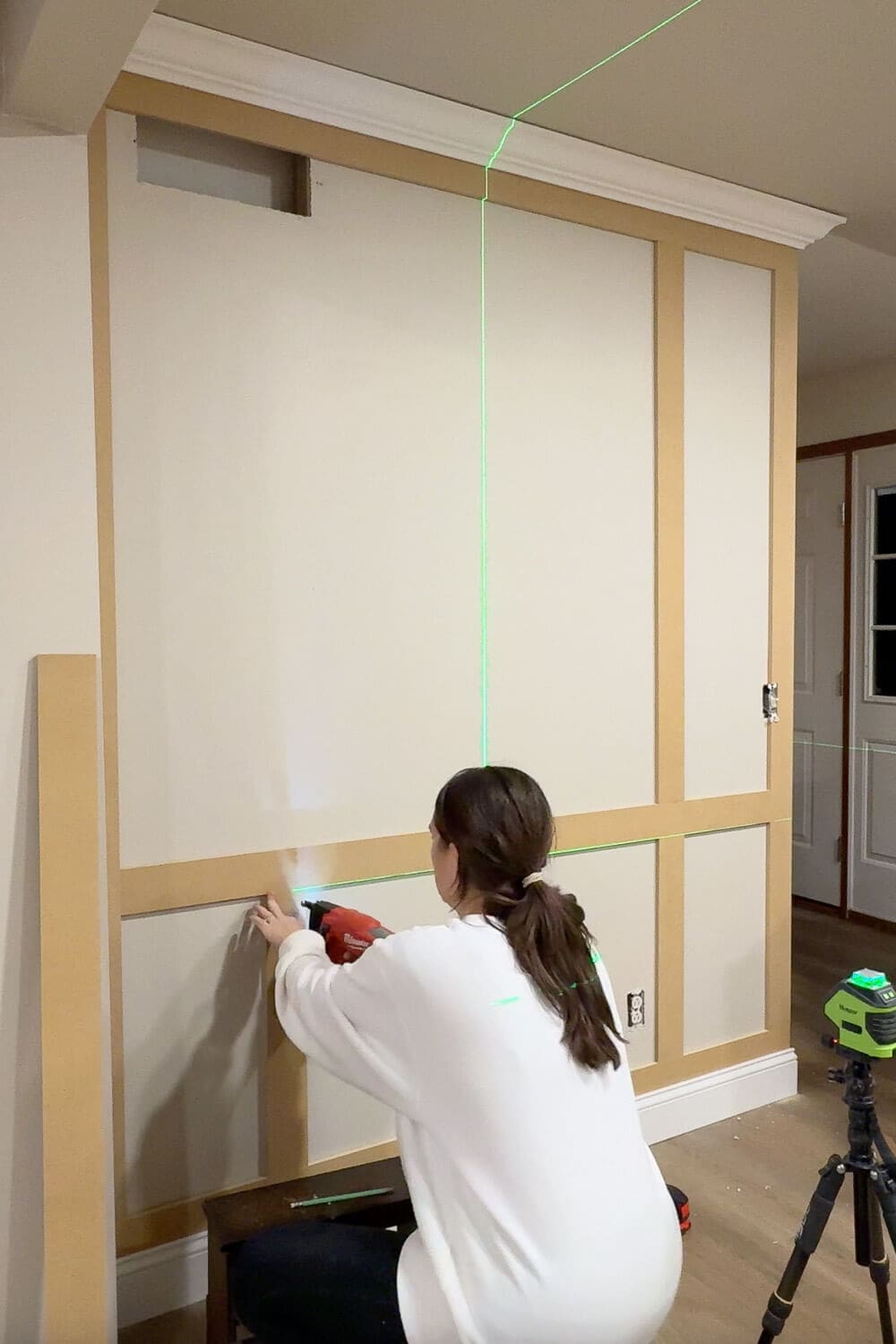 Installing picture frame molding on a freshly skim coated wall, using a laser level to keep the trim lines straight on the smooth, texture-free surface