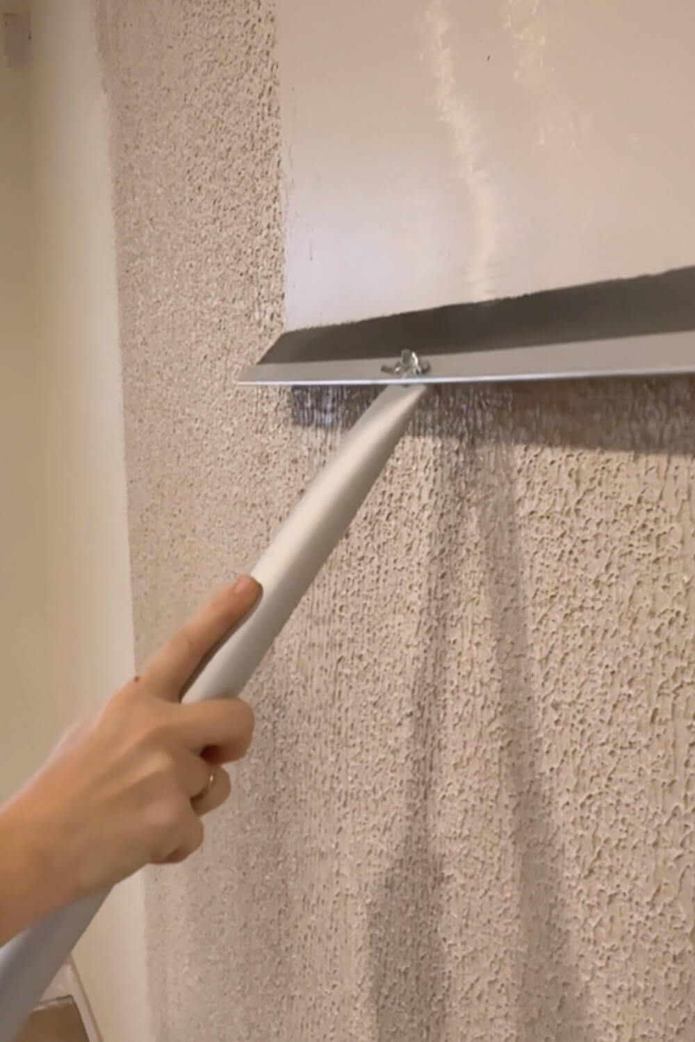 Pulling a wide drywall trowel over rolled-on joint compound to skim coat a textured wall and knock down the texture