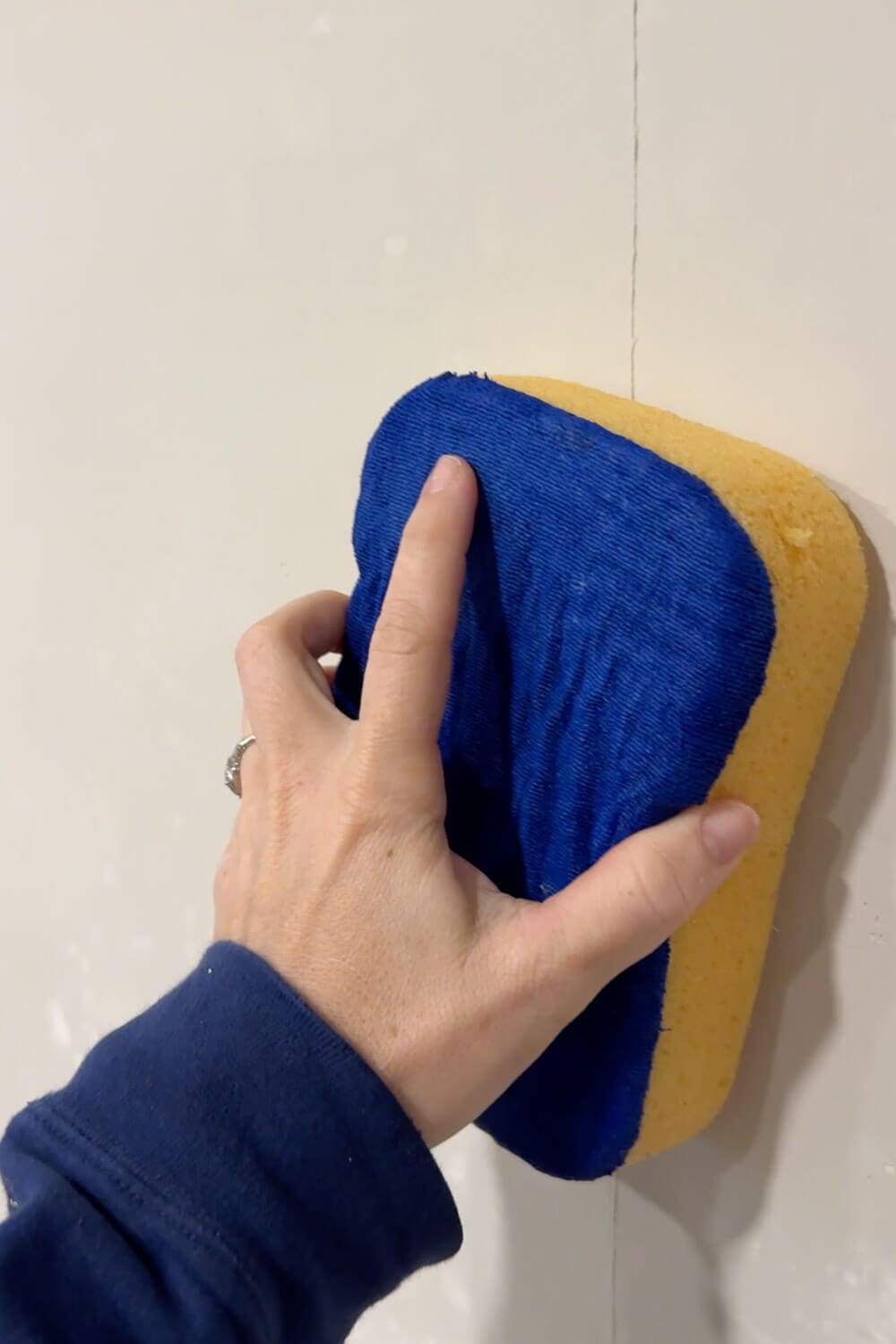 Using a damp sponge to smooth skim coat joint compound and remove trowel lines for a flatter, smoother wall finish
