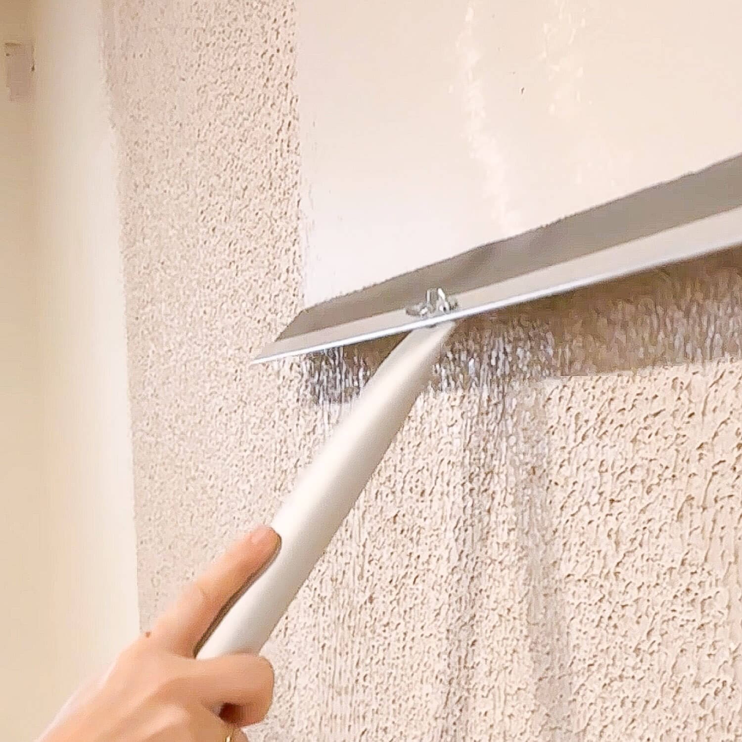 Using a wide drywall trowel to skim coat over heavy wall texture, flattening the surface as the joint compound is pulled smooth