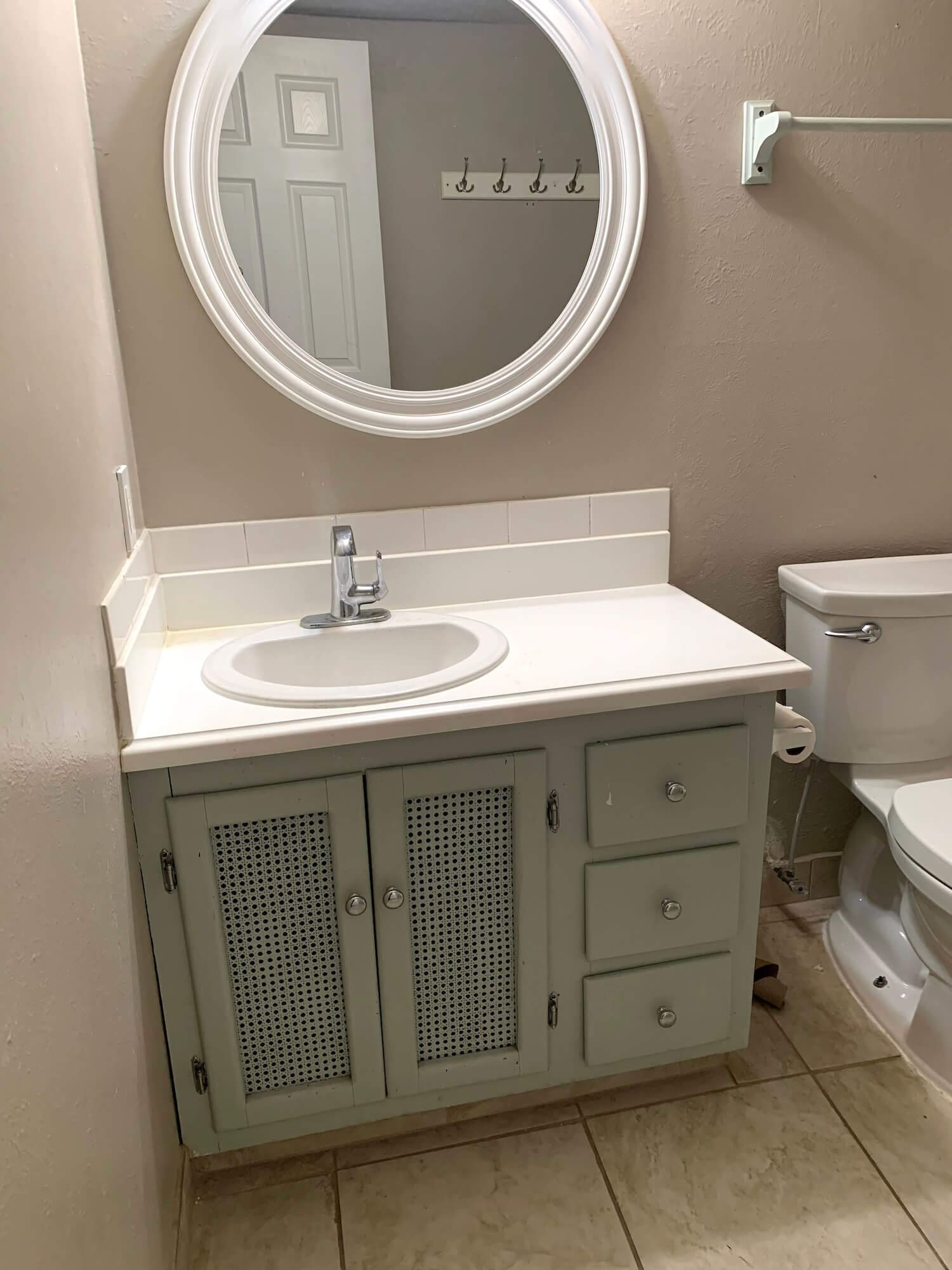 Before photo of the bathroom vanity and round mirror with beige walls and outdated finishes.