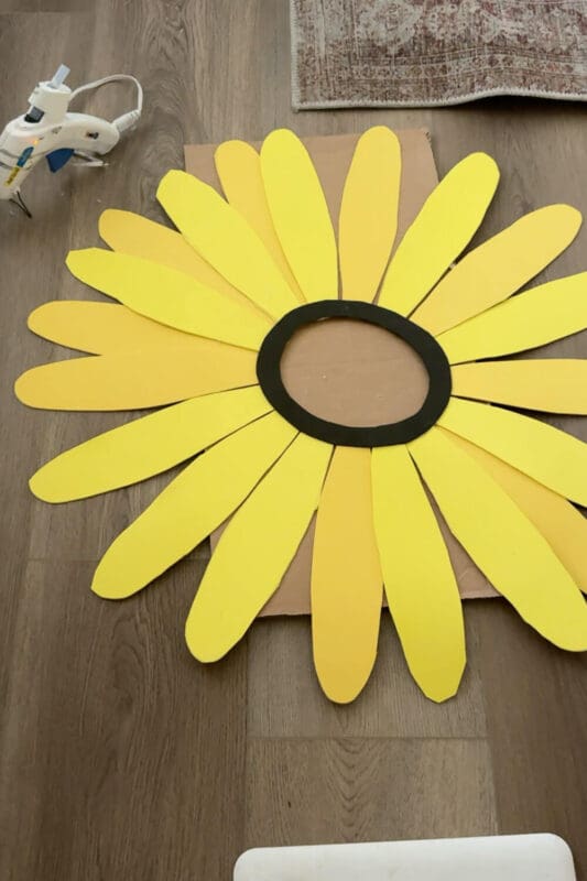 Sunflower headpiece layout with long yellow cardstock petals and a black face ring on a cardboard base, ready to glue for an easy no sew flower costume.