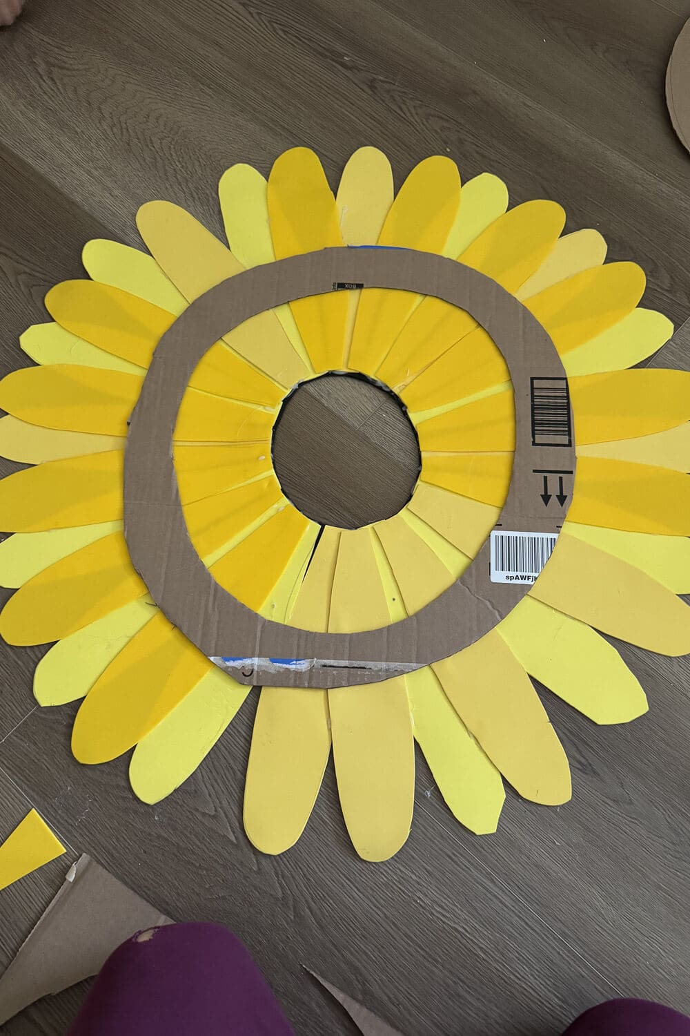 Sunflower headpiece being made for Halloween, in progress with layered yellow cardstock petals glued under a cardboard face ring, showing the circular opening and petal spacing.
