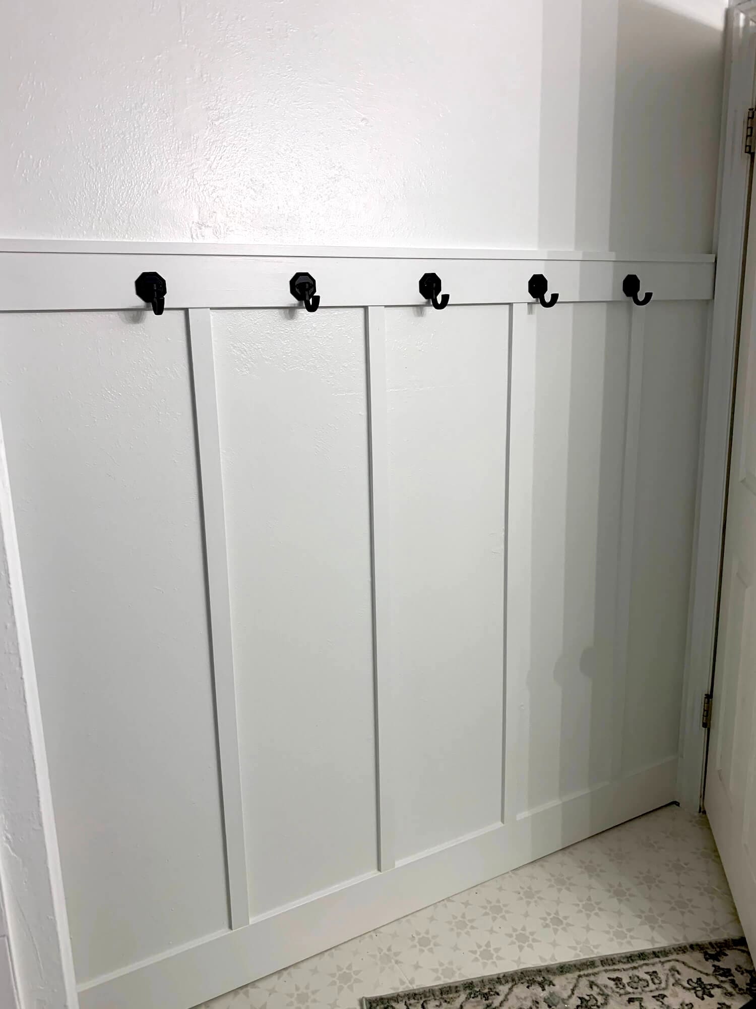 Close-up of a white wall with a simple top rail and black hooks