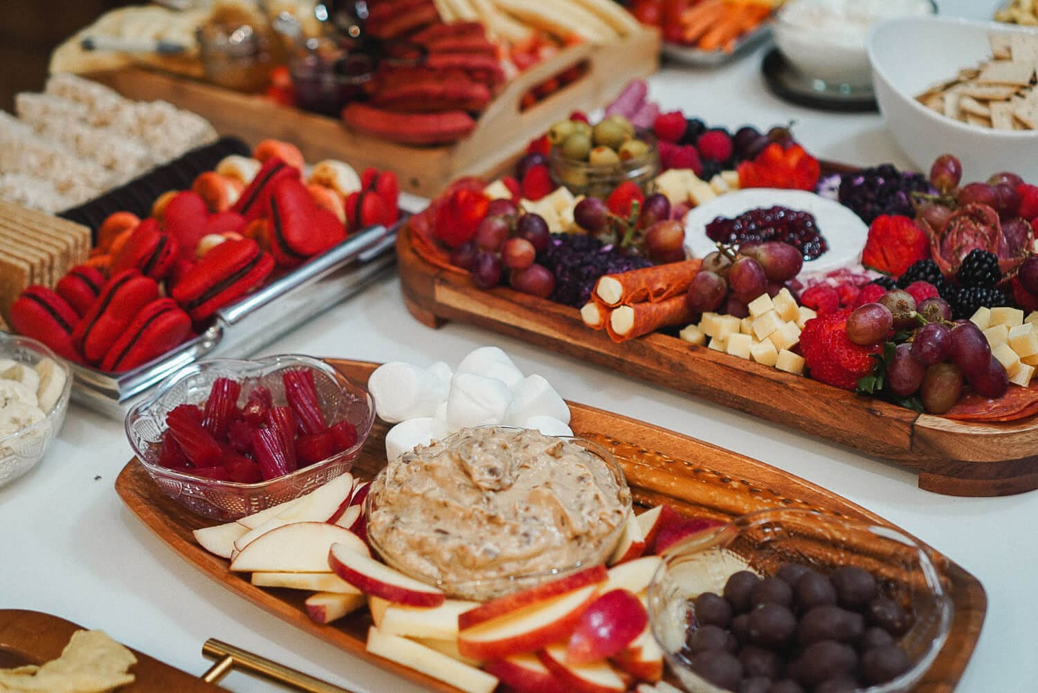 Apple dip tray with sliced apples, marshmallows, and pretzels in the foreground, set among assorted charcuterie and dessert boards on a party table.