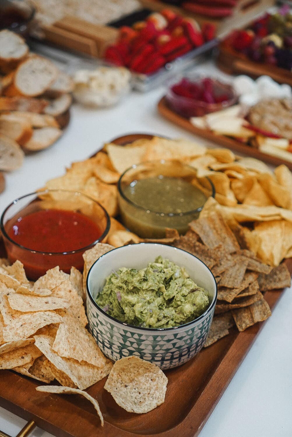 Chips and dips tray with guacamole, red salsa, salsa verde, and an assortment of tortilla chips and whole-grain crisps—easy potluck appetizer for a crowd.