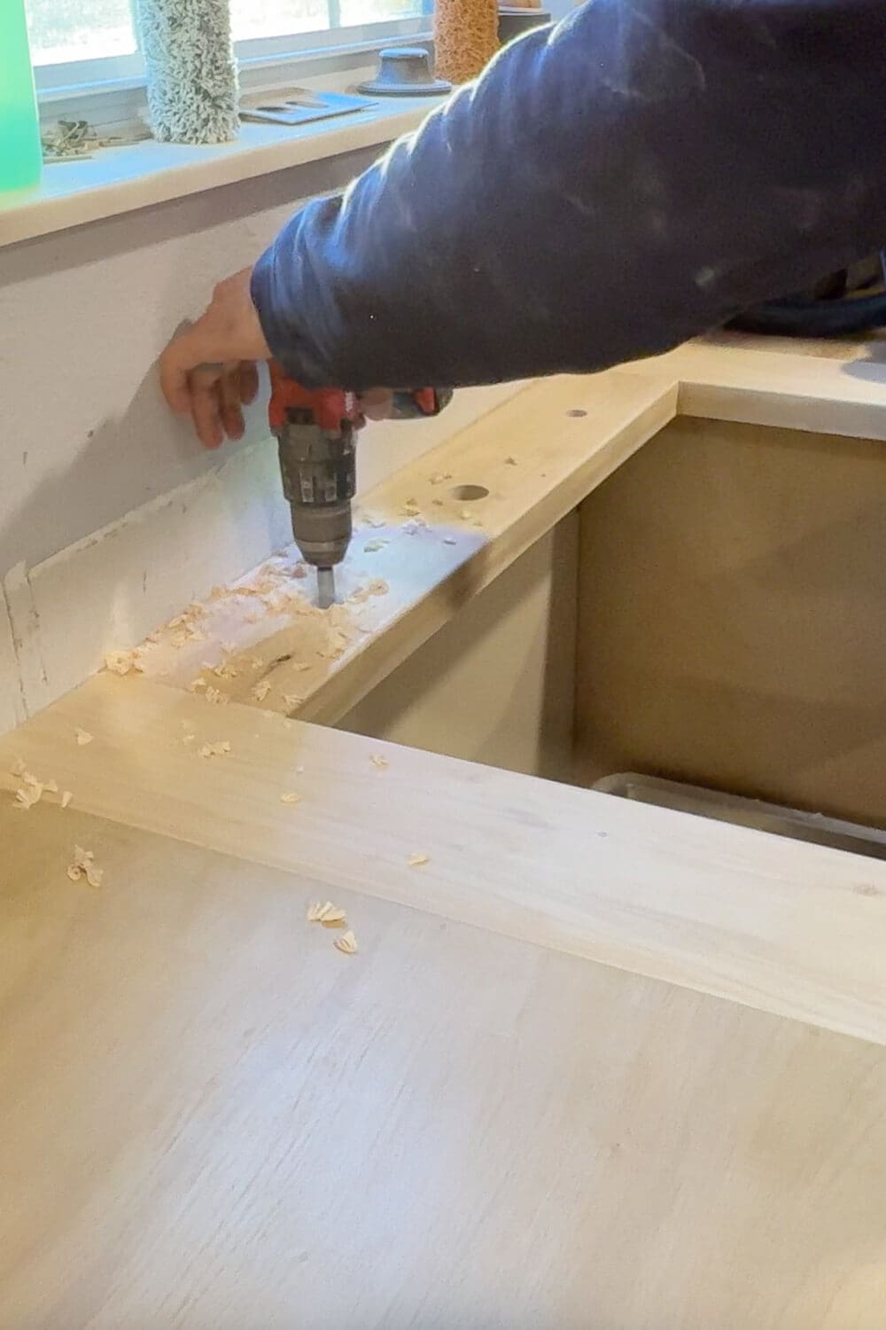 Person using a power drill with a hole saw bit to cut into new plywood kitchen counters to create holes for the kitchen faucet.