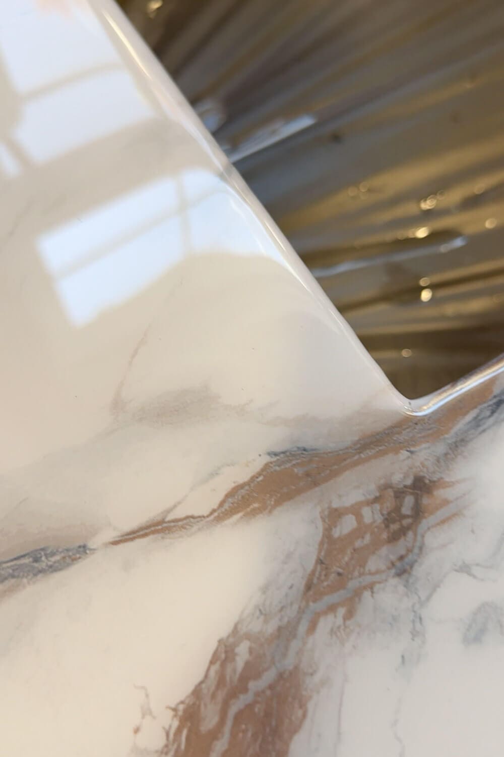 Detail of smooth epoxy edge on DIY marble-look countertops, highlighting the seamless transition from faux marble contact paper into the undermount stainless steel kitchen sink.