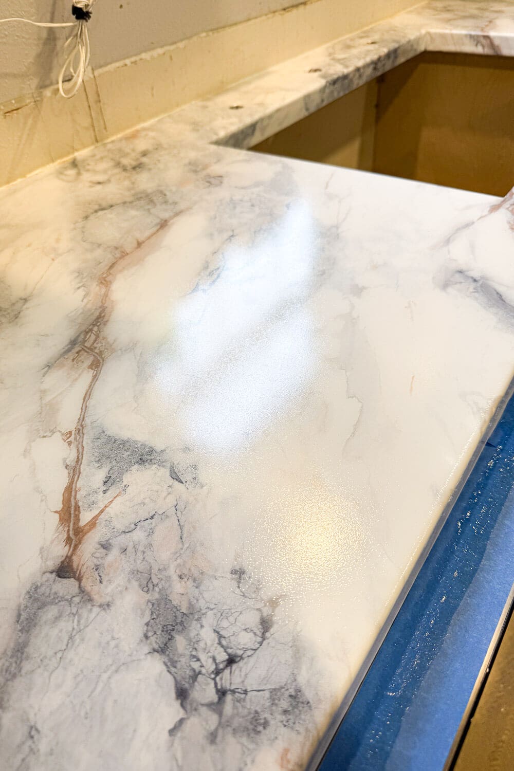 DIY countertops with faux marble finish in progress, marble-look contact paper and clear epoxy resin on plywood with sink cutout and taped edges in a budget kitchen remodel.