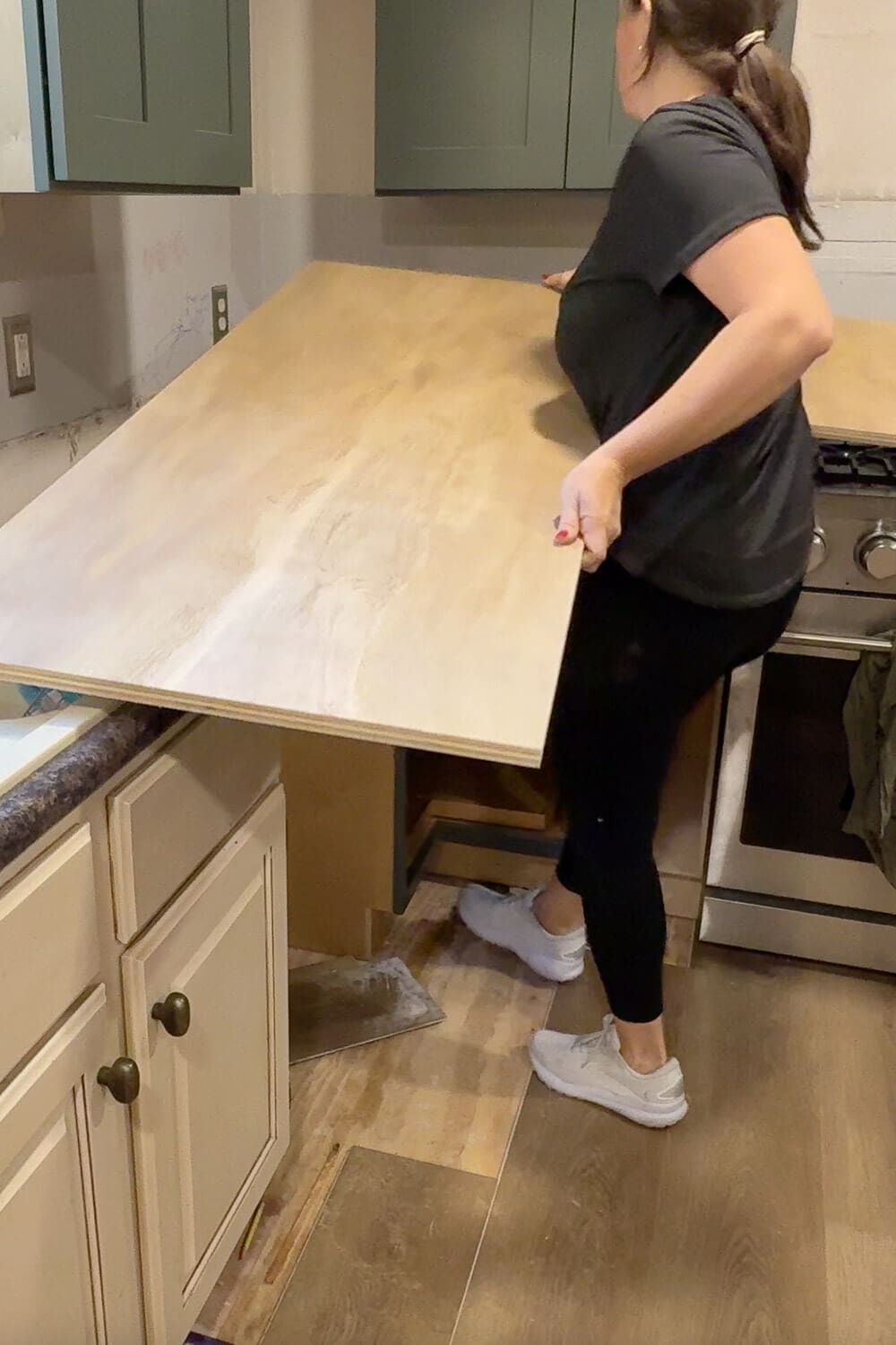Lifting a large sheet of plywood onto kitchen cabinets while installing DIY countertops, showing the raw plywood base before the faux marble and epoxy finish.