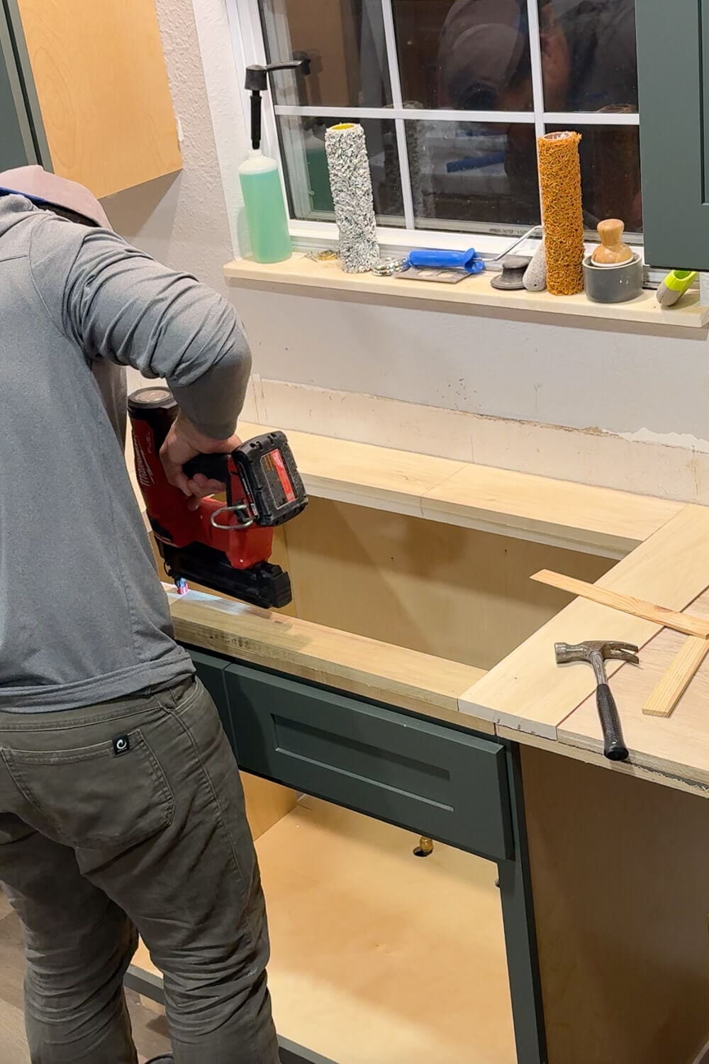Using a cordless nail gun to attach the front edge to plywood counters, creating a sturdy base around the kitchen sink.