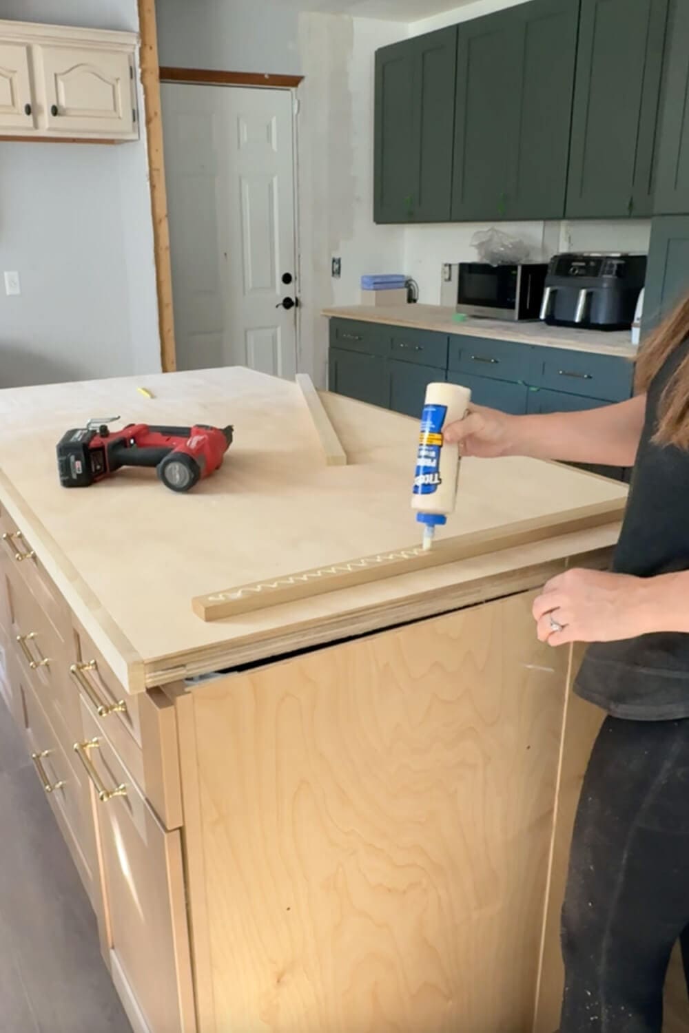 Adding wood glue to a trim board on a plywood kitchen island while building budget-friendly counters, creating a thicker edge profile before the marble-look contact paper and epoxy finish.
