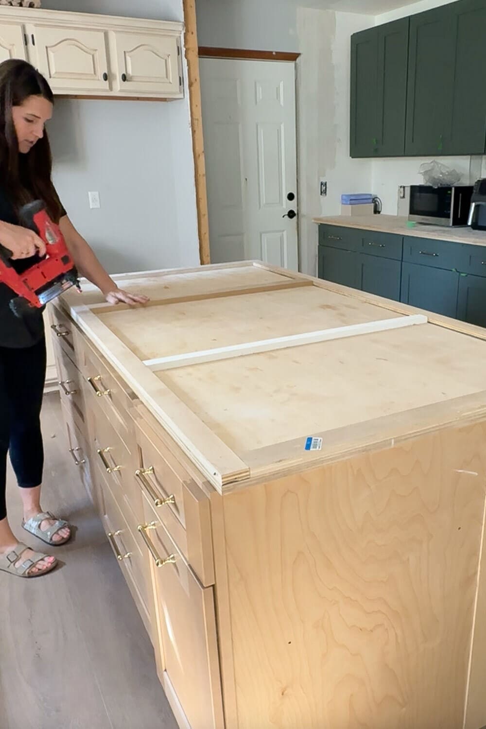 Attaching wood trim to a large plywood kitchen island while building DIY countertops, creating a thick edge profile before wrapping the island in faux marble and epoxy.