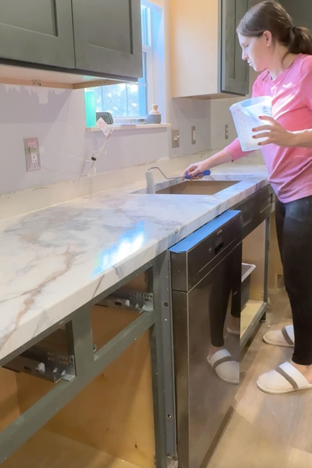 Pouring and rolling clear epoxy over DIY countertops that look like marble, sealing the faux marble contact paper around the kitchen sink for a durable, glossy finish.