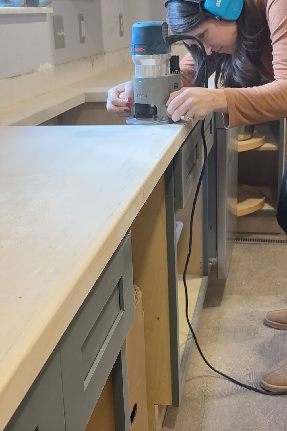 Woman using a Bosch router to round over the edge of new plywood kitchen counters.