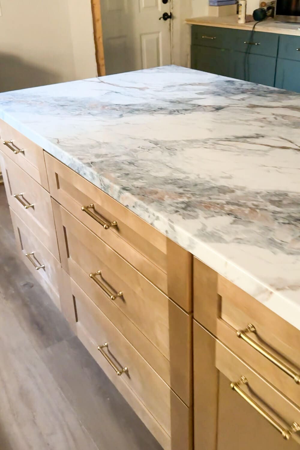 DIY countertops that look like marble on a large kitchen island, showing white and gray faux marble contact paper with subtle veining over plywood cabinets with brass drawer pulls.