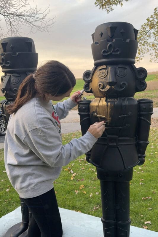 Woman brushing Rub n Buff onto a black giant nutcracker, adding the first antique bronze layer for a DIY Christmas makeover.
