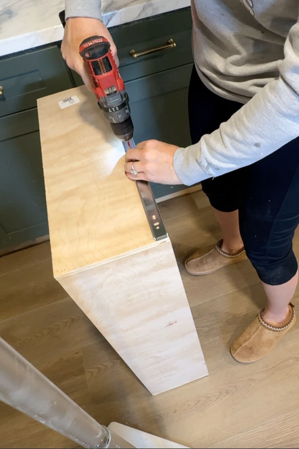Installing a drawer slide on the side of a plywood pull-out drawer box using a drill before adding custom pots and pans storage dividers.