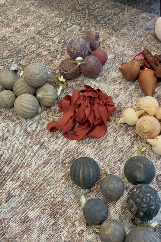 Neutral and black textured Christmas ornaments with satin ribbon laid out on a patterned rug, ready to be finished with Rub n Buff.