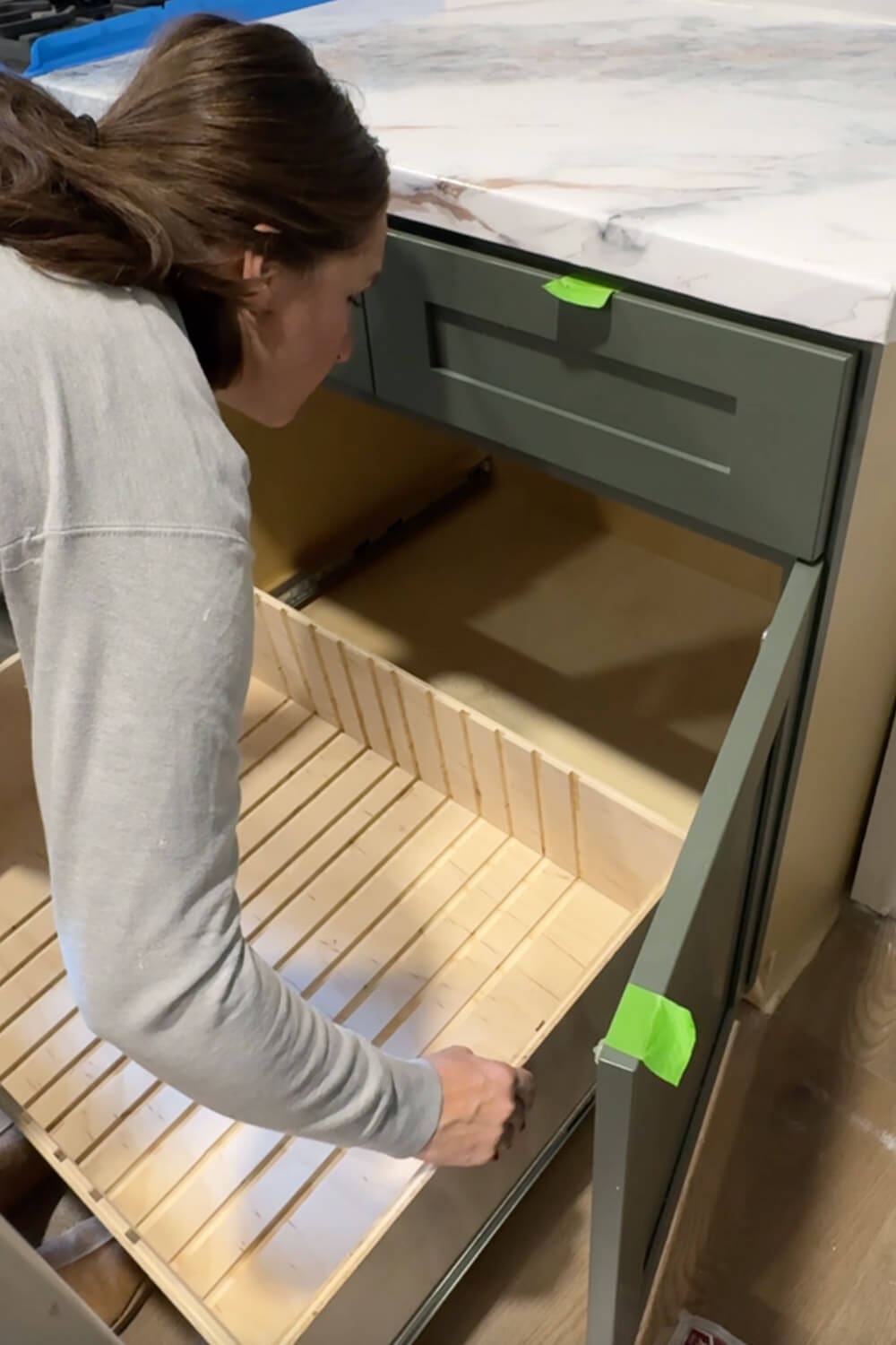 Woman is putting in an empty slide-out plywood drawer with routed grooves, testing the fit inside a lower kitchen cabinet before adding dividers for pots and pans storage.
