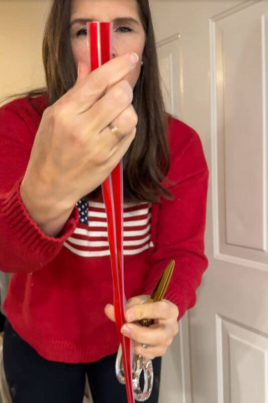 DIY blogger holding a clear front door weatherstripping strip with red backing before installation