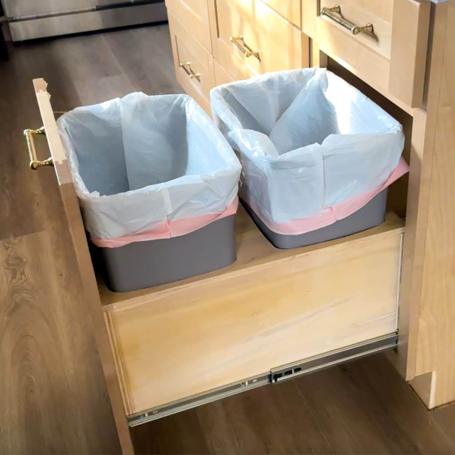 DIY pull out double trash can cabinet fully extended from a light wood kitchen base cabinet, showing two gray bins lined with trash bags sitting on a custom-built plywood platform mounted to heavy-duty drawer slides.
