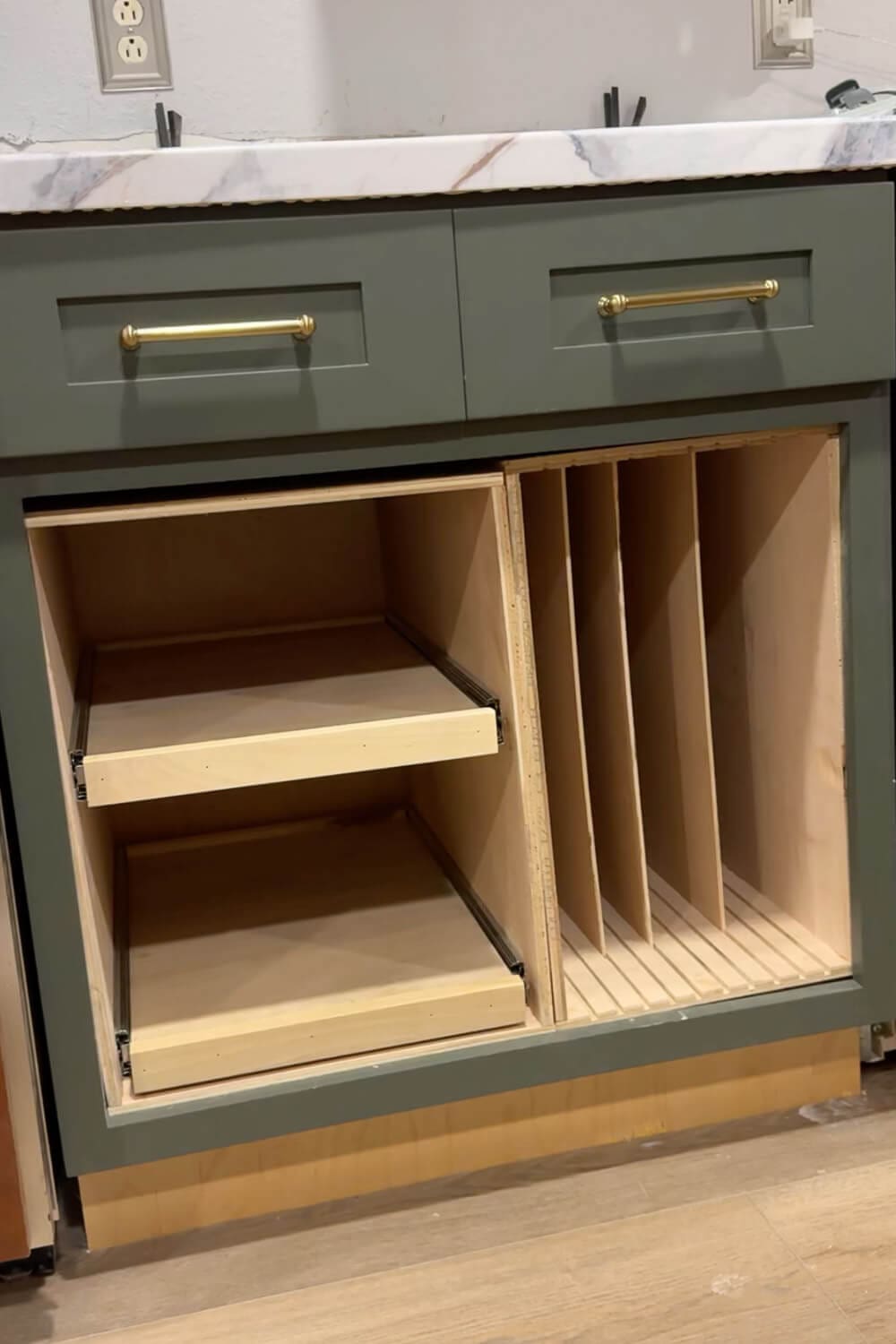 Built in plywood cabinet organizer with two pull out shelves on the left for organizing Tupperware food storage containers and vertical dividers for cutting boards and baking sheets on the right in a green kitchen cabinet.