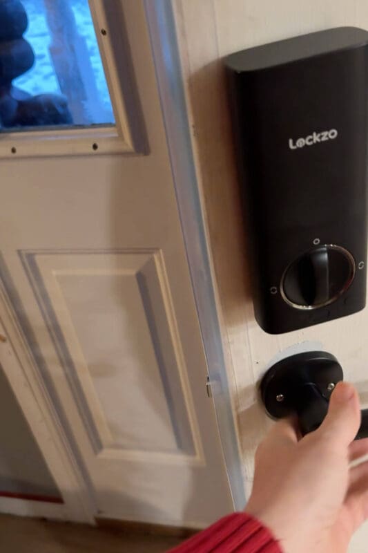 Close up of a front door with clear weatherstripping installed next to a black smart lock as the handle turns to close the door