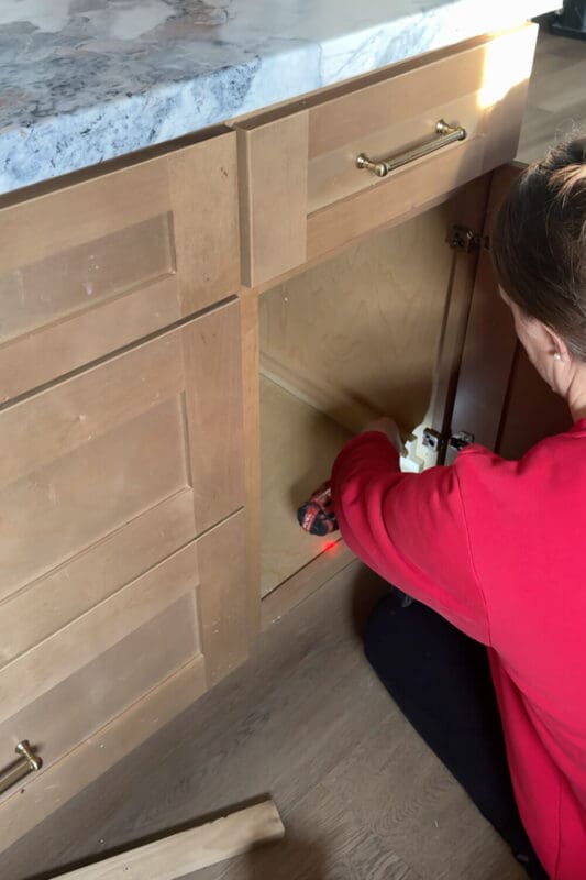 DIYer installing support spacers for drawer slides to add a DIY garbage bin pull-out in this kitchen.