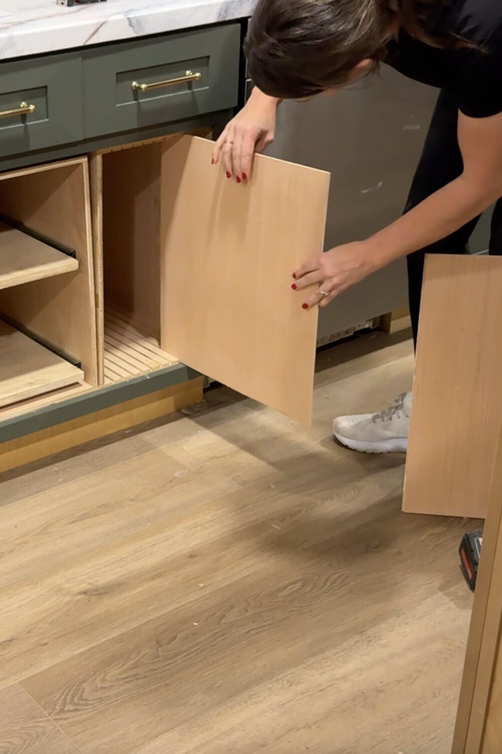 Placing a plywood divider panel into the slotted base of a DIY sheet pan organizer inside a lower kitchen cabinet