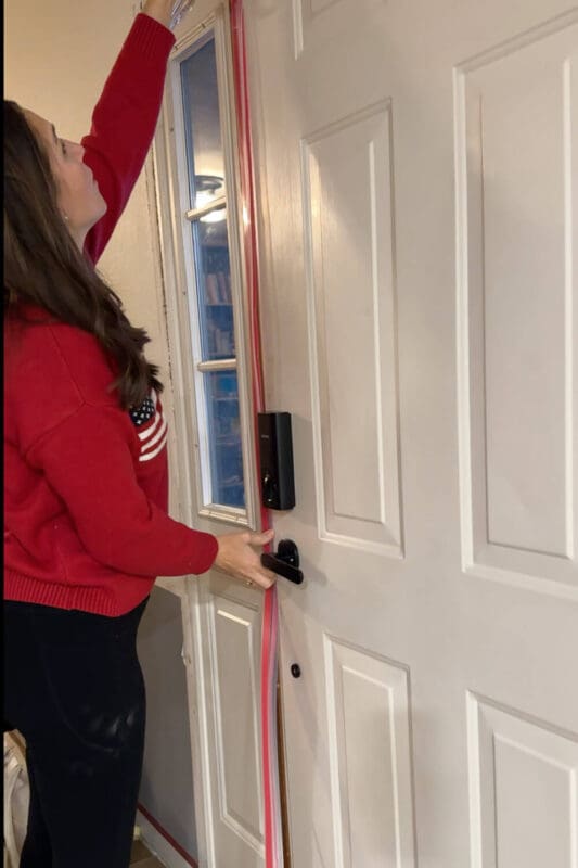 DIY blogger lining up clear weatherstripping along the side of a white front door to seal a drafty gap