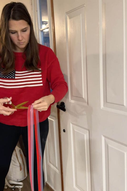DIY blogger measuring and cutting a clear weatherstripping strip with red backing for a front door