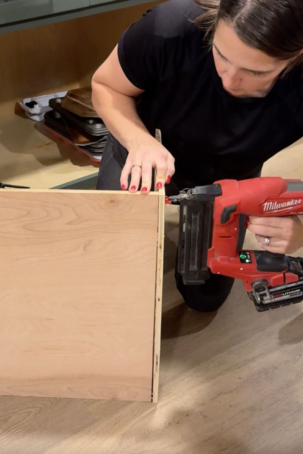 Using a brad nailer to attach the side panel to the plywood box for a custom DIY sheet pan organizer cabinet insert