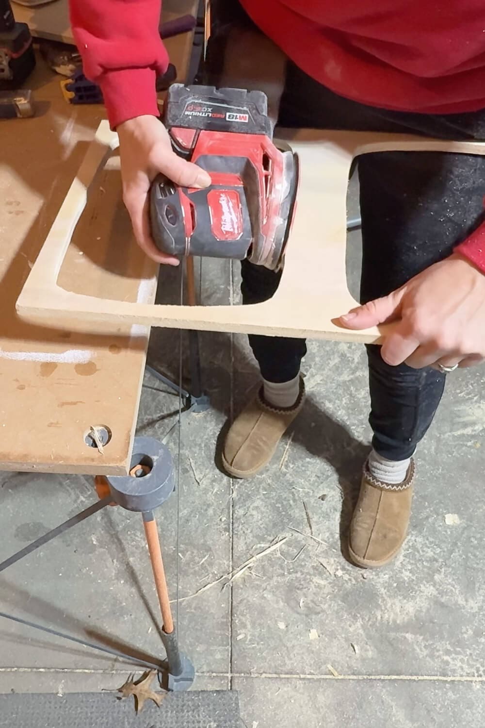 Sanding the inside edge of a freshly cut plywood opening with a cordless sander to smooth the top frame for a custom pull out garbage bin holder.