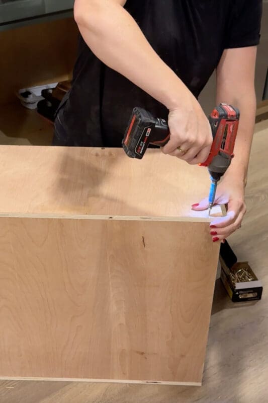 Driving screws into the corner of a plywood box to build a sturdy DIY vertical storage cabinet insert