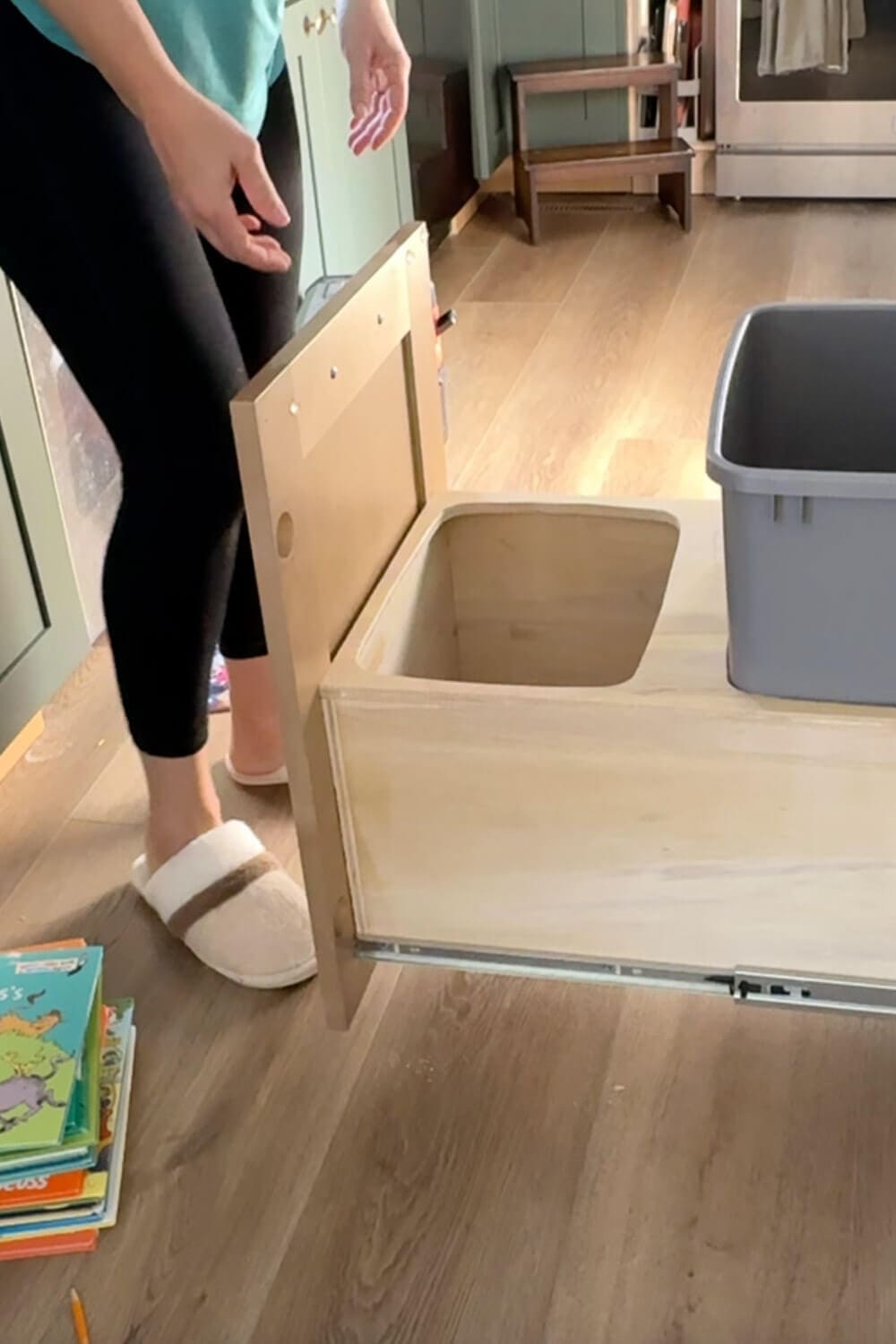 Cabinet door attached to the front of the plywood double trash can drawer, propped on kids’ books while testing the slide movement for the new DIY pull out trash can cabinet.