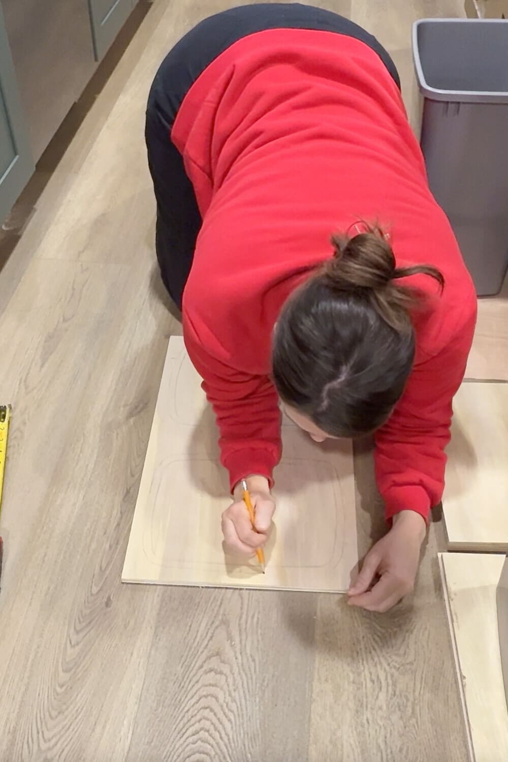 Drawing rounded rectangles on a plywood board to map out cutouts for the bins, planning the top panel for a DIY pull out double trash can cabinet.