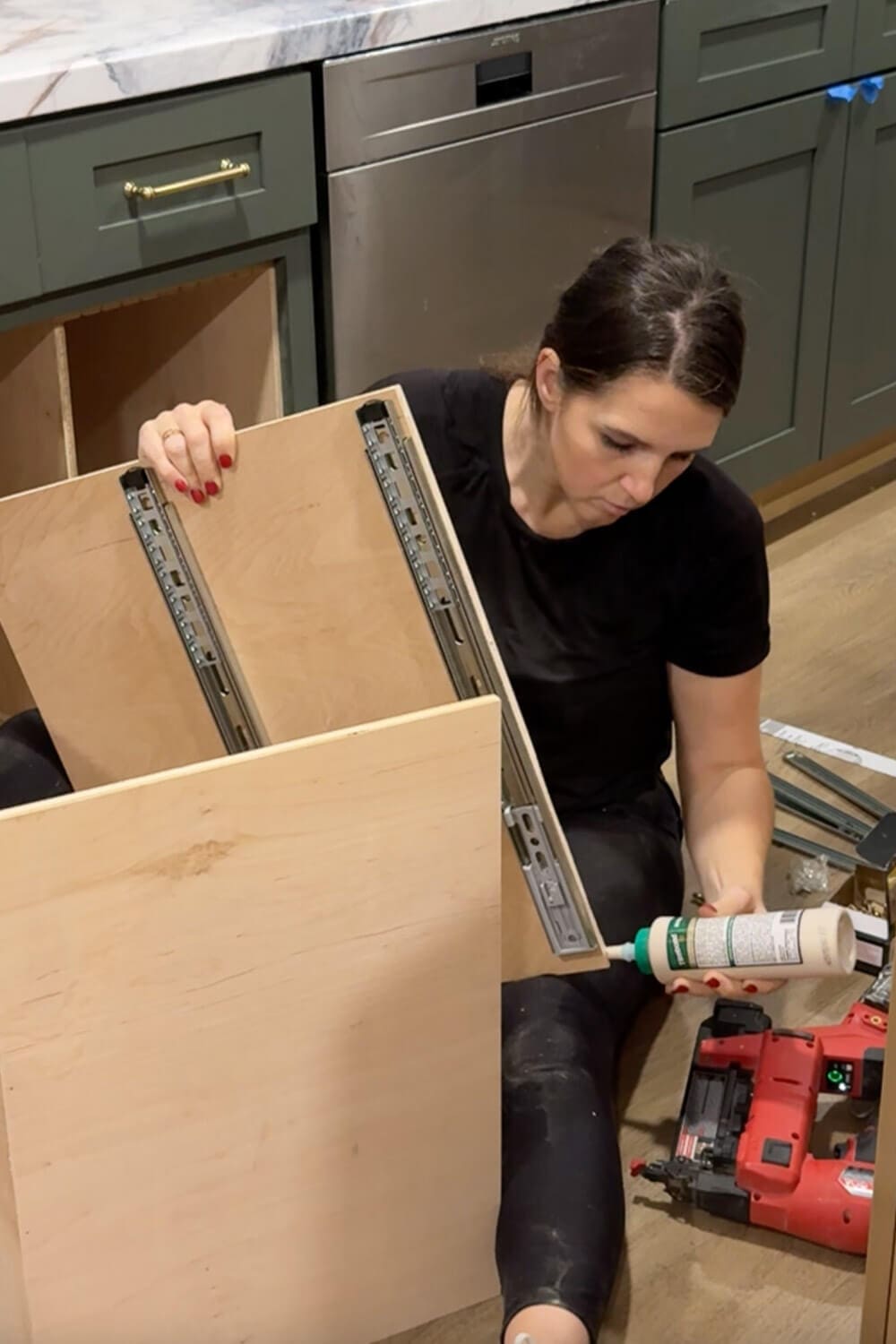 Woman applying wood glue to the edge of a plywood panel with drawer slides attached while building a custom pull-out organizer for glass food storage containers.